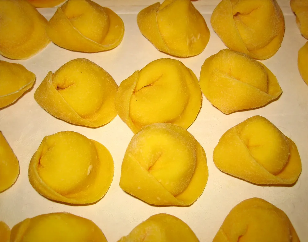 Pasta fresca all'uovo ripiena, chiusa a mano e infarinata su un vassoio
