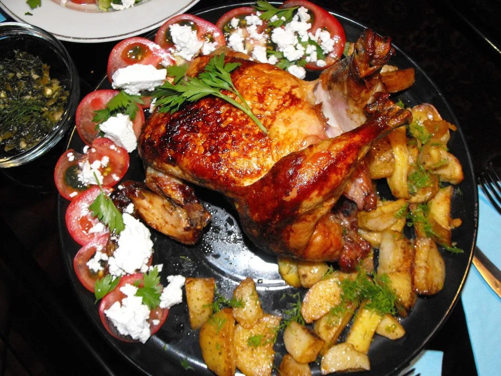 Pollo intero arrosto dorato servito con patate al forno su un piatto da portata