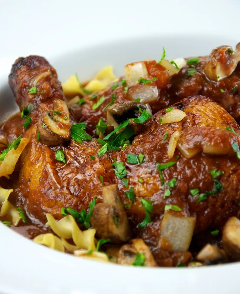 Pollo in umido con sugo di pomodoro, funghi e cipolla servito in un piatto fondo